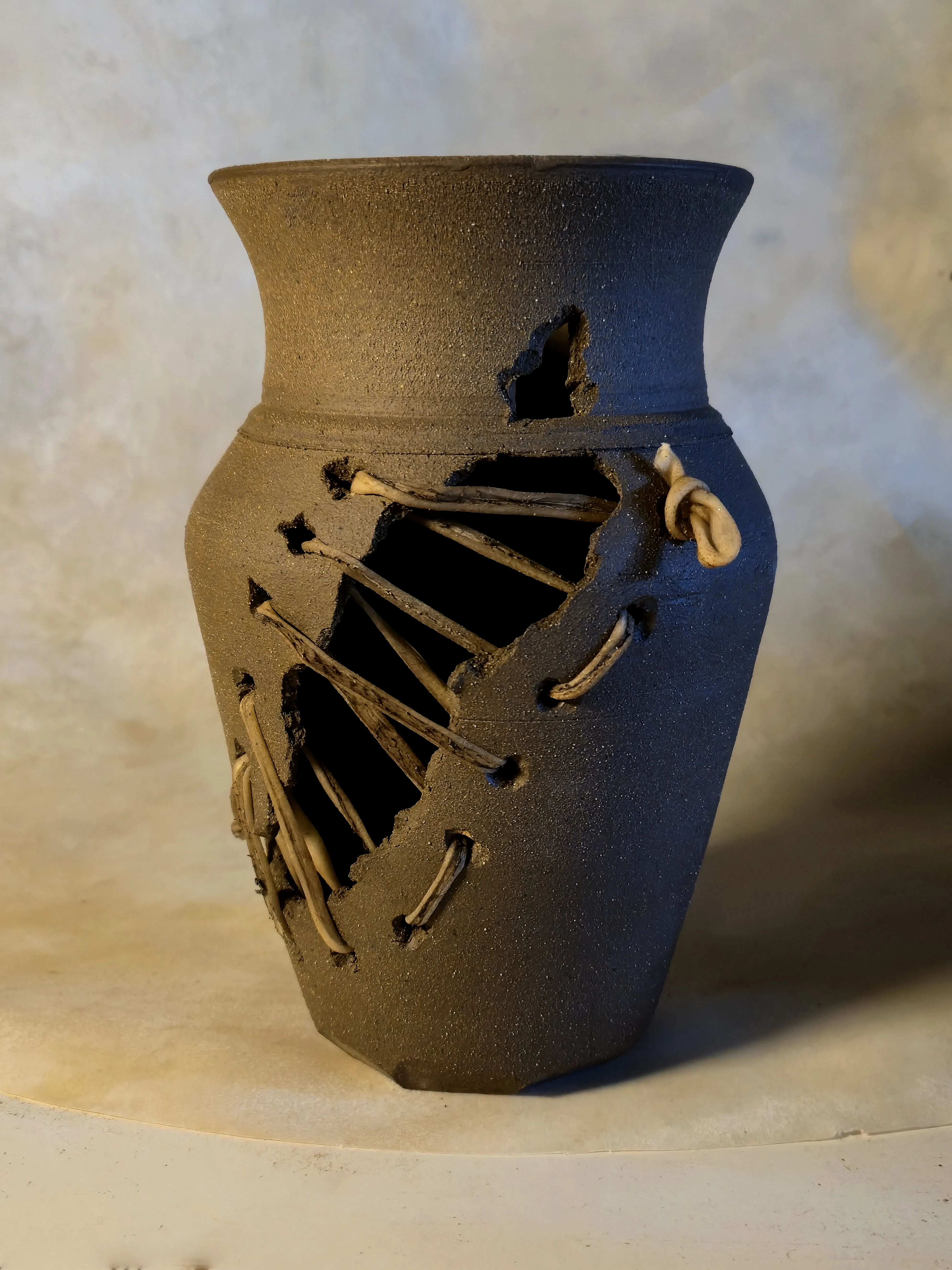 A dark vessel with a diagonal tear crossed by tight rawhide stitches.