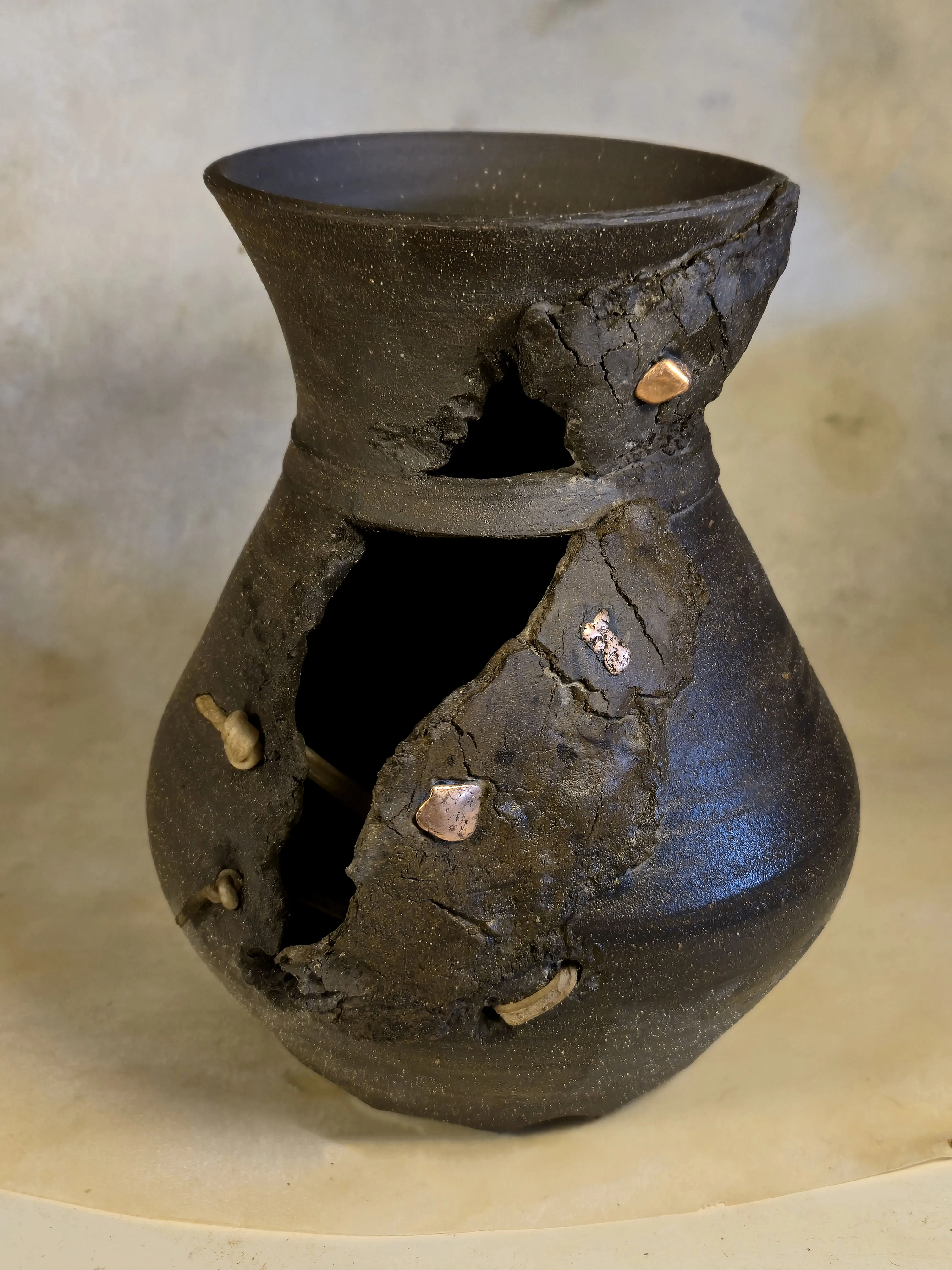 A black vessel split open down its side, with nuggets of native copper set into the broken edge.