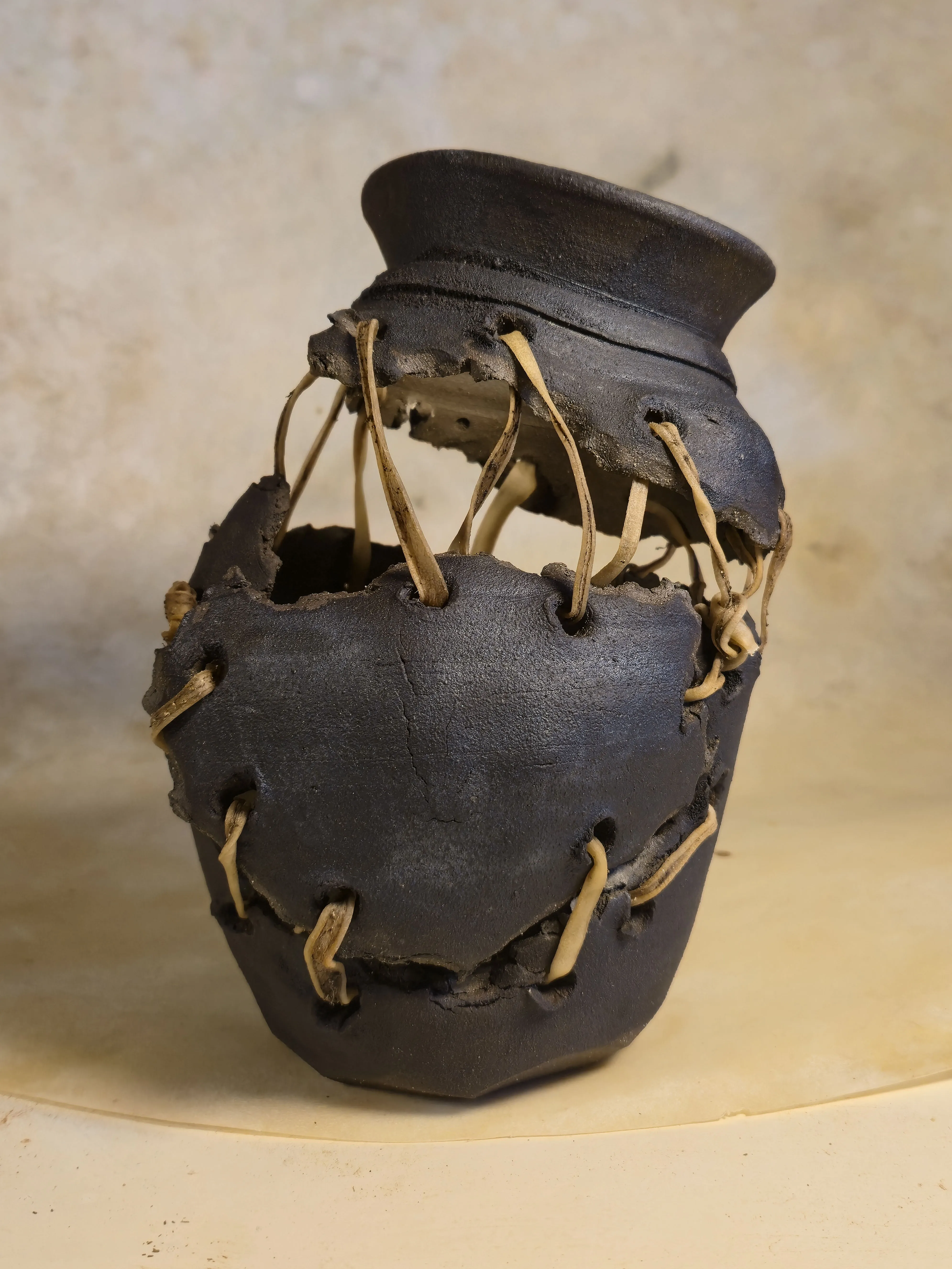 A vessel broken into separated bands, suspended and held together by loops of rawhide.